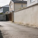 Petite rue privee partagee bordee de murs, maisons mitoyennes en arriere-plan